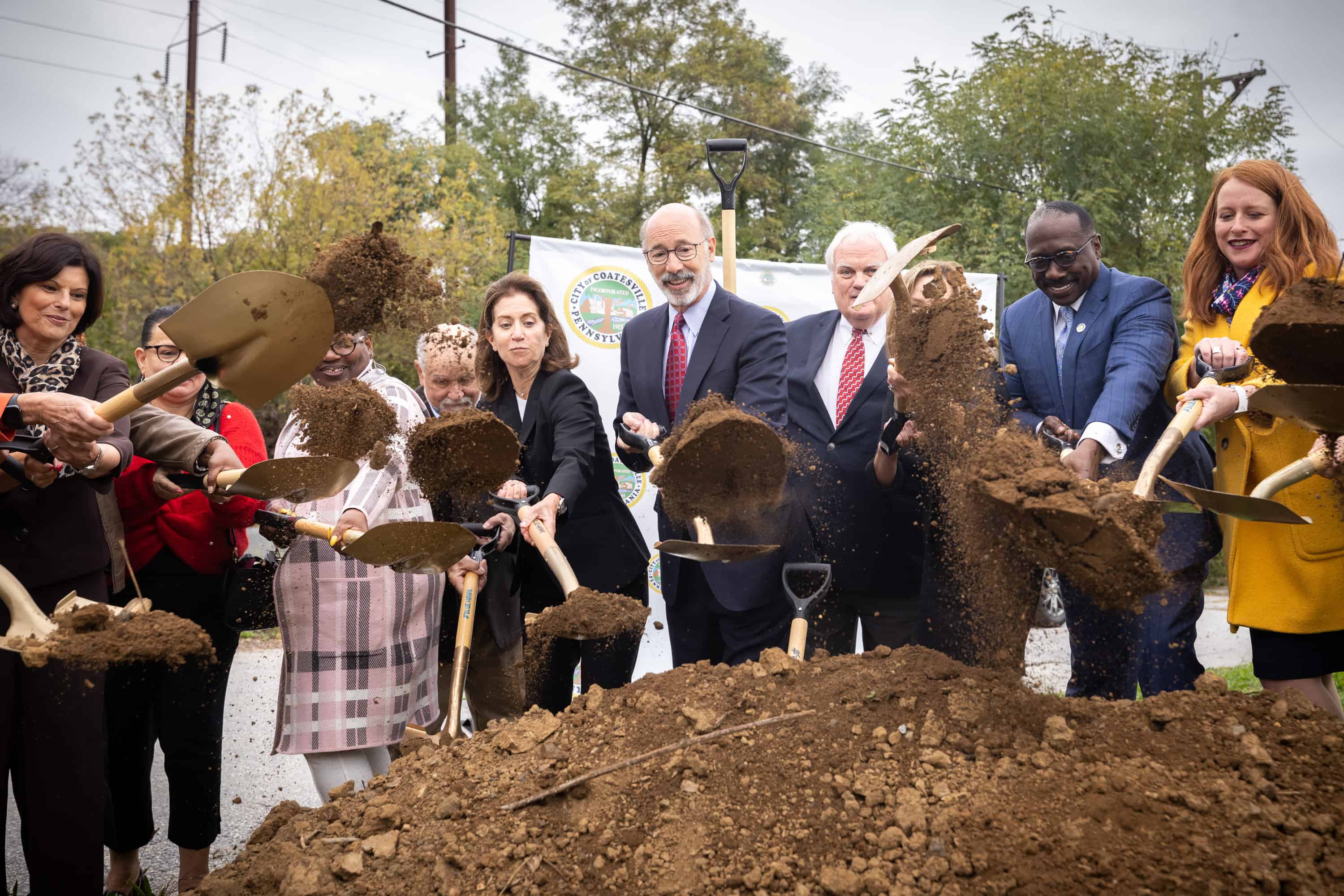 Governor Wolf and other officials break ground at the new Coatesville train station. Their shovels fling dirt toward the camera.